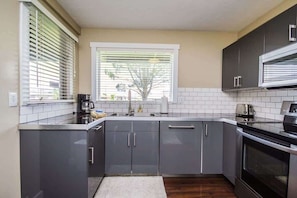 Een moderne keuken met grijze kastjes, een roestvrijstalen afzuigkap en een raam met zonwering.