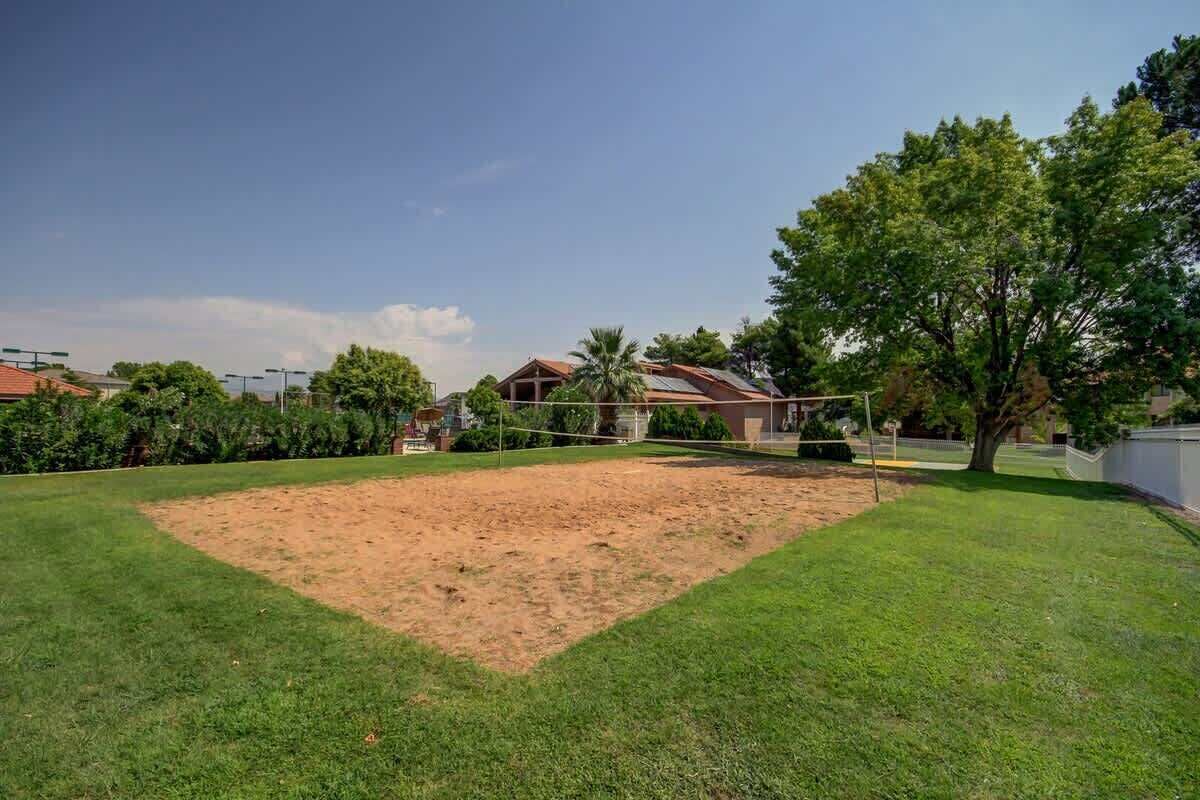 Ein Garten mit Volleyballnetz, Sandfläche und einem Haus im Hintergrund.