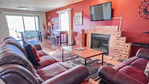 A living room with a fireplace, a TV mounted on the wall, and a dining area with a table and chairs.