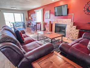 A living room with a fireplace, a TV mounted on the wall, and a dining area with a table and chairs.