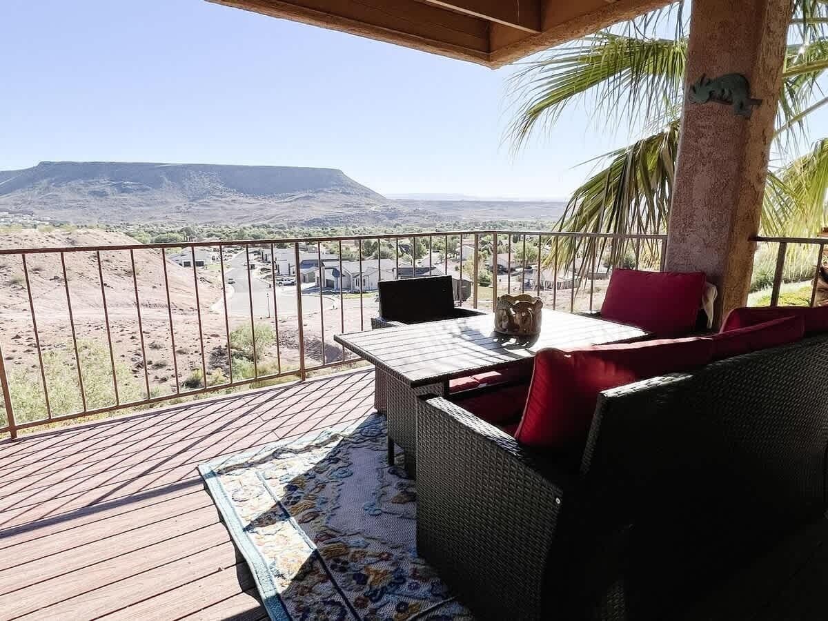 Un balcon agrémenté de meubles en osier, un ordinateur portable et une vue sur un paysage désertique.