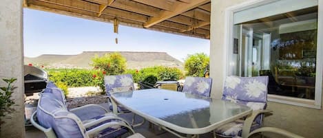 Un patio al aire libre con una mesa y sillas de vidrio, una parrilla de barbacoa y vistas a la montaña.