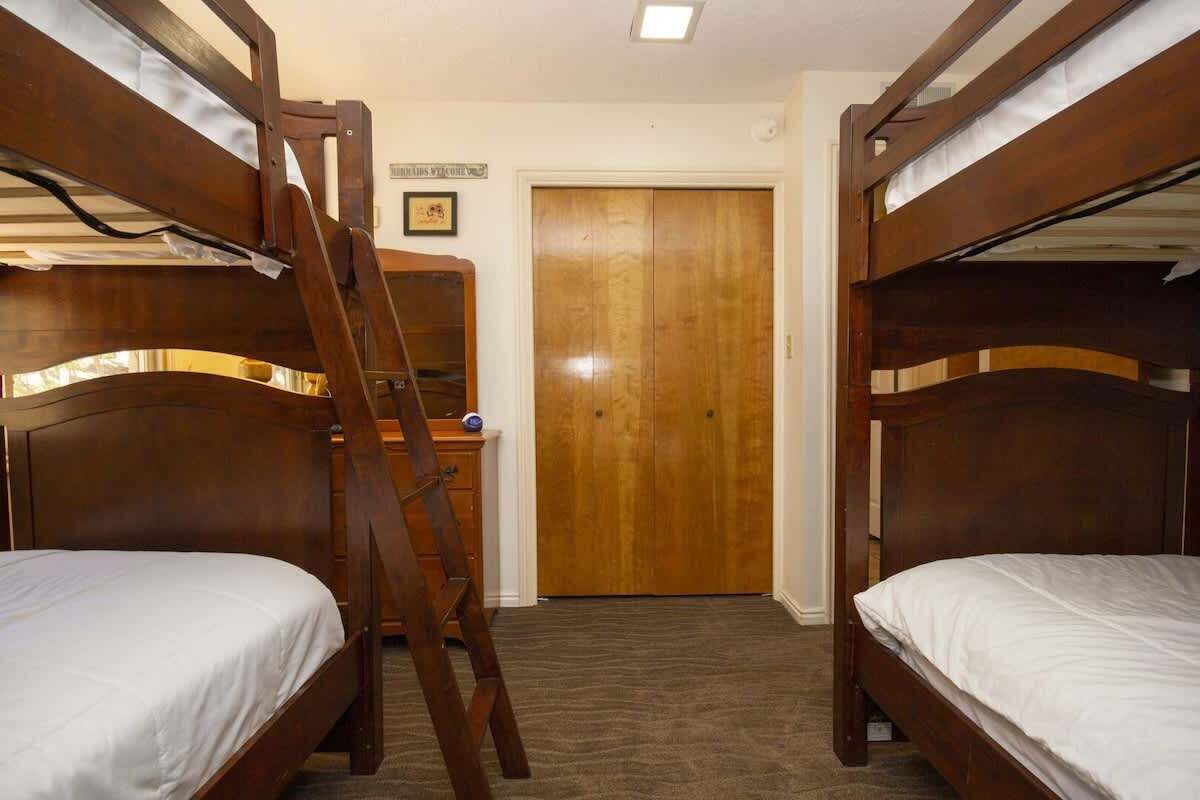 A room with two bunk beds, a wooden ladder, a dresser, and a door.