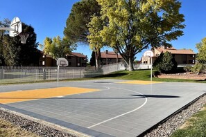 An outdoor basketball court with a fence, trees, and residential buildings in the background. - Sports Village Resort #X3 | All Amenities Included (Saint George)