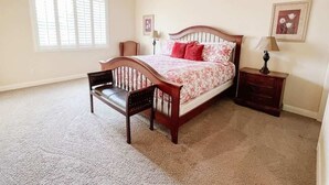 A bedroom with a bed, a chair, a nightstand, a lamp, a ceiling fan, and a window with blinds.