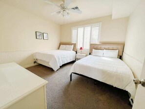 A bedroom with two single beds, a ceiling fan, a window with blinds, and a bedside table with a lamp.