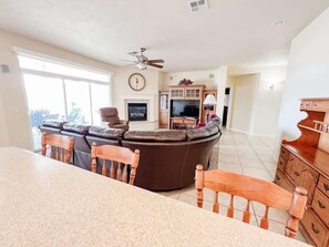 A spacious living room with a large brown leather sofa, a wooden dining table with chairs, a television, and a fireplace.