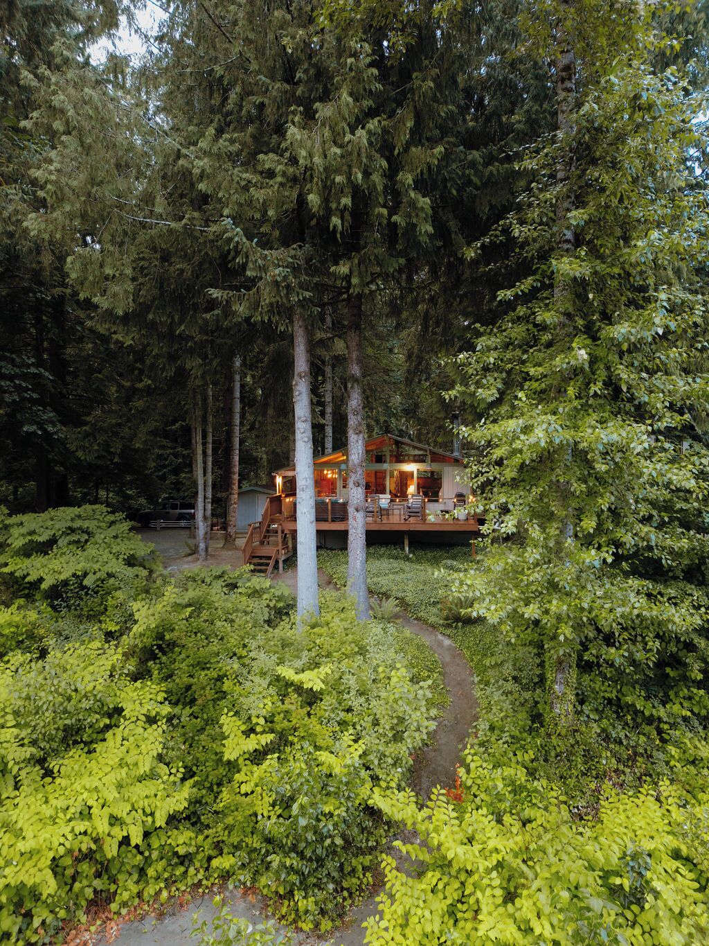 A cabin surrounded by dense forest with a wooden deck and outdoor seating area.