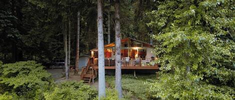 A cabin surrounded by dense forest with a wooden deck and outdoor seating area.