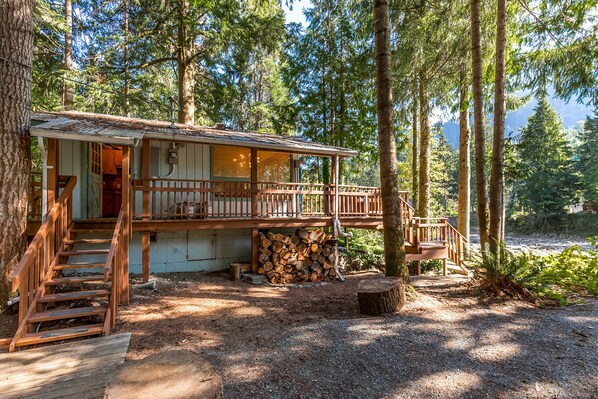 A cabin with a wooden deck and stairs leading to a covered entrance. - Stargazer Studio - riverfront pet-friendly cabin (Gold Bar)