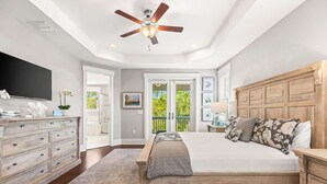 A bedroom with a bed, wooden headboard, a ceiling fan, a dresser, a TV, and a view of the outdoors. - Coastal Elegance at NatureWalk: Modern Retreat Minutes from the beach! (Santa Rosa Beach)