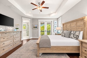 A bedroom with a wooden bed, a ceiling fan, a TV, and a view of the outdoors. - Nature and the Beach - 5BR/3BA Naturewalk Home - Sleeps 10 - Bikes (Santa Rosa Beach)