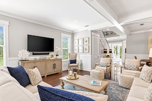 A spacious living room with a large flat-screen TV, comfortable seating, a wooden cabinet, and a staircase leading to another level. - Nature and the Beach - 5BR/3BA Naturewalk Home - Sleeps 10 - Bikes (Santa Rosa Beach)