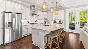 A modern kitchen with white cabinetry, stainless steel appliances, a central island with bar stools, and pendant lighting. - Coastal Elegance at NatureWalk: Modern Retreat Minutes from the beach! (Santa Rosa Beach)