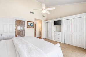 A bedroom with a bed, a ceiling fan, a TV, and white wardrobes.