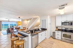 A modern kitchen with white cabinets, stainless steel appliances, and a central island with stools. - Blue Tide 6B - Beachfront 3BR/3BA Seagrove Beach Condo - Sleeps 8 - Beach Setup Included (Inlet Beach)