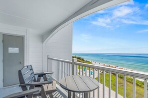 A balcony with a view of the ocean, a door with a sign, and a table with chairs.