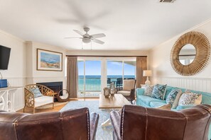 A living room with a view of the ocean, a ceiling fan, a fireplace, and a large mirror. - Blue Tide 6B - Beachfront 3BR/3BA Seagrove Beach Condo - Sleeps 8 - Beach Setup Included (Inlet Beach)
