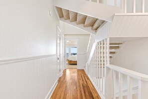 A hallway with wooden flooring, white walls, and a staircase with a textured ceiling. - Blue Tide 6B - Beachfront 3BR/3BA Seagrove Beach Condo - Sleeps 8 - Beach Setup Included (Inlet Beach)