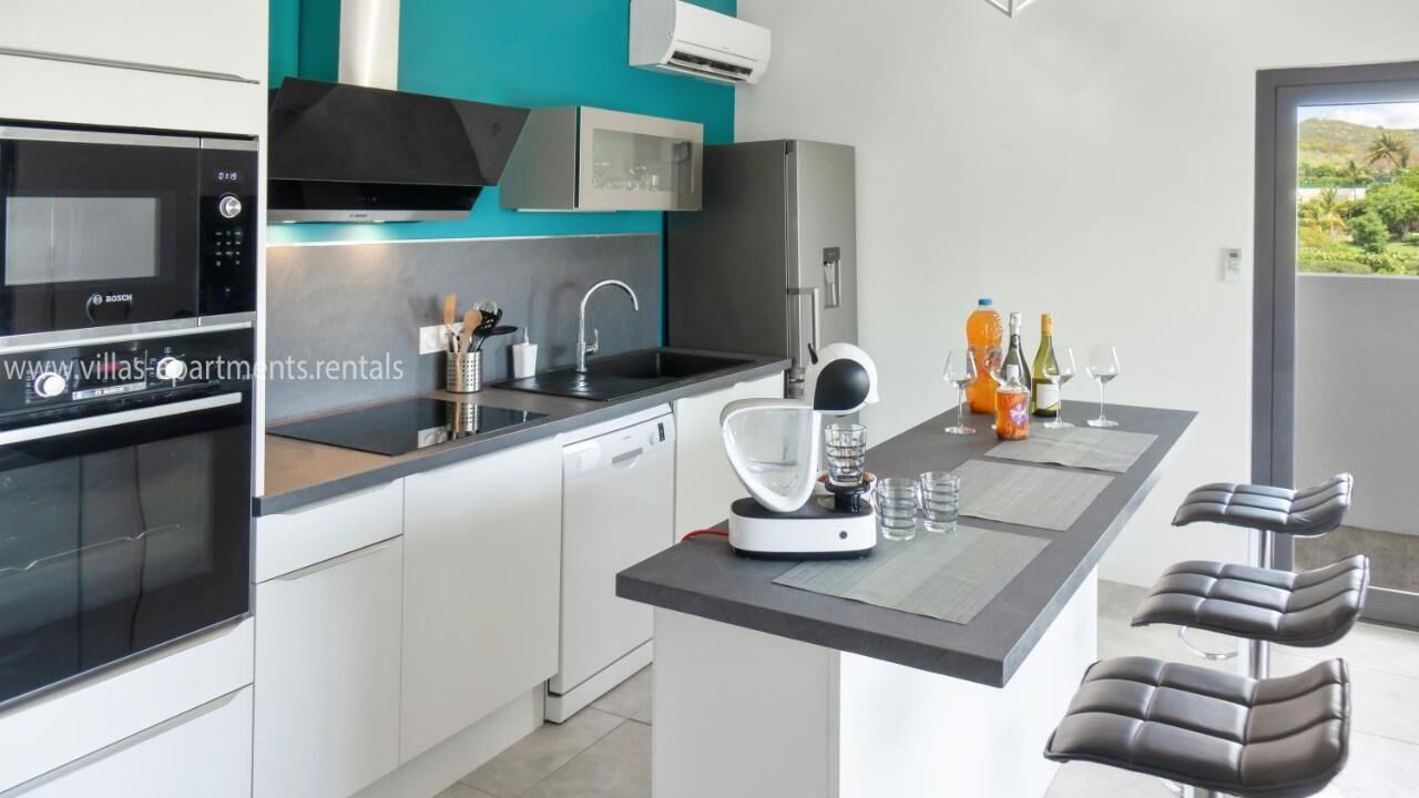 Une cuisine moderne équipée d’un four à micro-ondes Bosch, d’une machine à café et d’un évier. On peut voir des verres et des bouteilles de vin sur le comptoir.