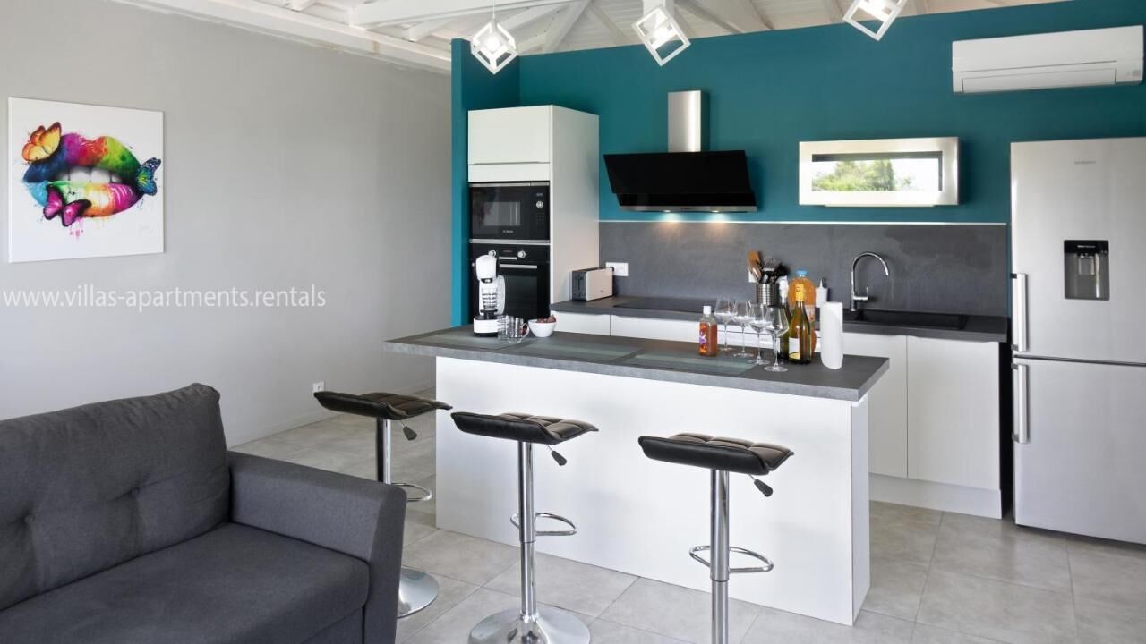 A modern kitchen with a central island, bar stools, a built-in oven, and a flat-screen TV.