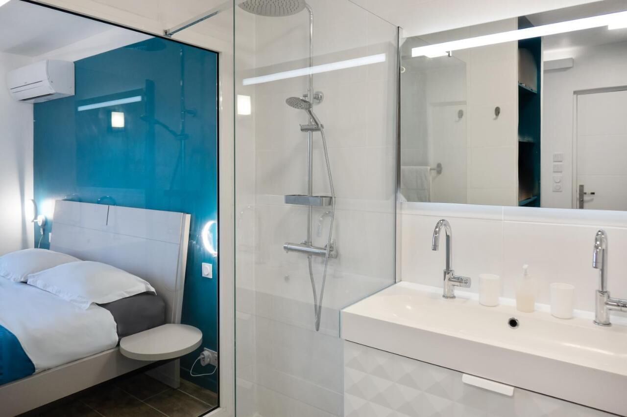 Une chambre d’hôtel moderne équipée d’un lit, d’une petite table de chevet, d’une douche en verre et d’un grand miroir dans la salle de bain.