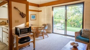 Ein Zimmer mit Esstisch, Stühlen, einem Fernseher auf einem Schrank, einer Gitarre und einer Glastür zum Garten.