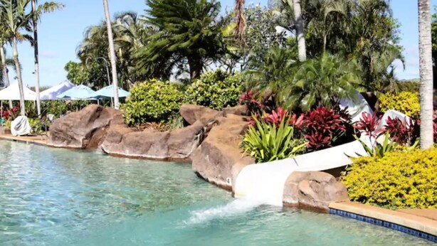 Ein Pool mit Wasserrutsche, umgeben von tropischen Pflanzen und Felsen.