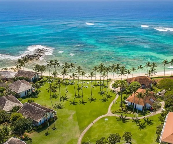 Luchtbeeld van een kustbezit met een strand, palmbomen en huizen met rieten daken.