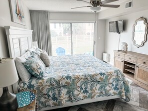 Een slaapkamer met een bed, een plafondventilator, een televisie, een spiegel en uitzicht op het buiten.