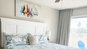 A bedroom with a bed, a ceiling fan, a painting, and a view of the outside. - Ground Floor, Close to Beach, Pet Friendly Free Wifi/Beach Svs 2 Pools, New Mgmt (Miramar Beach)