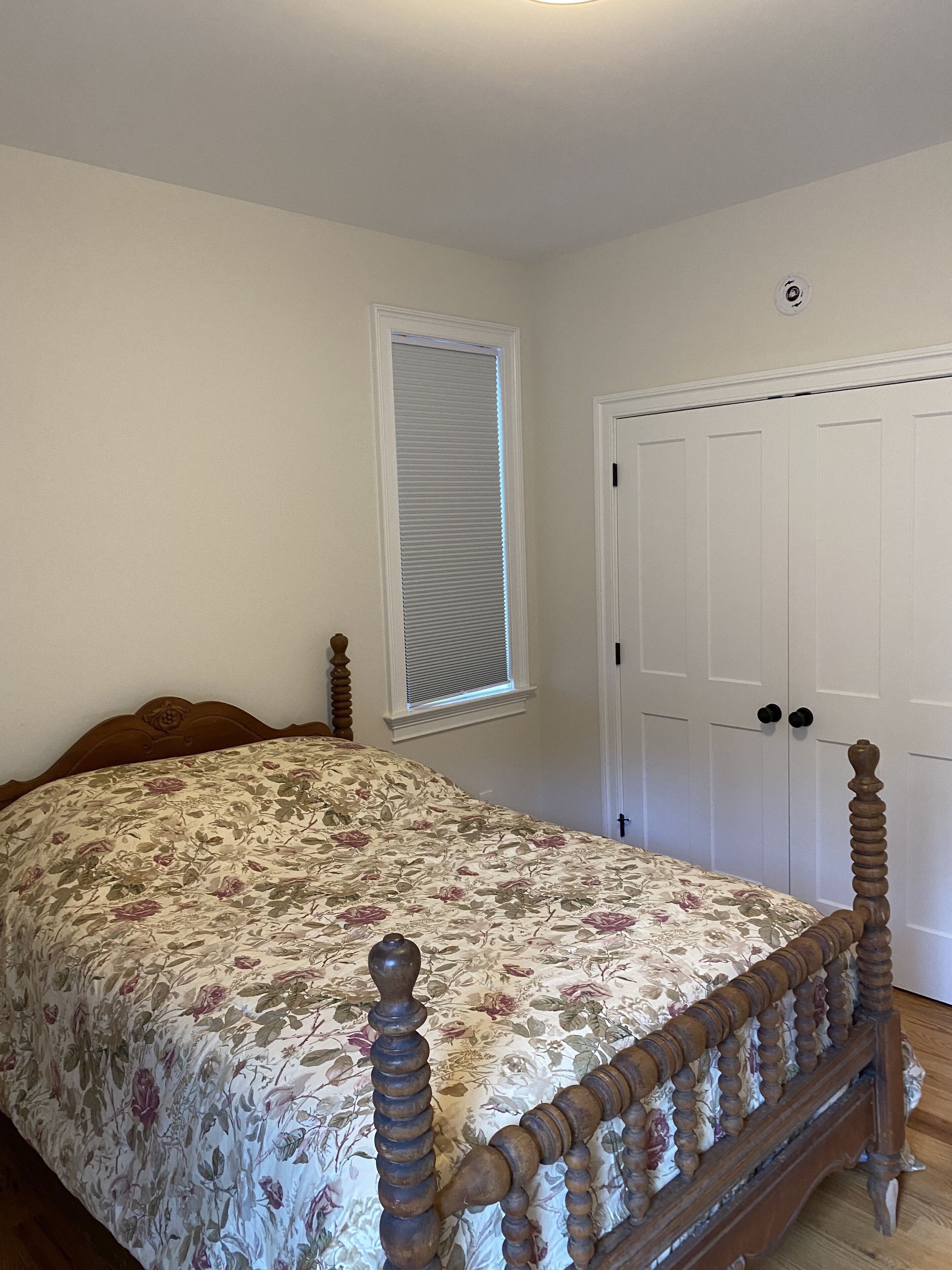 Un dormitorio con una cama de madera con dosel, una ventana con persianas y una puerta blanca con dos pomos.
