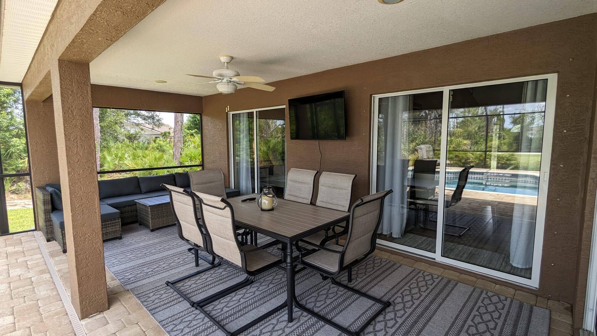 A covered patio with a table and chairs, a sofa, and a TV mounted on the wall.
