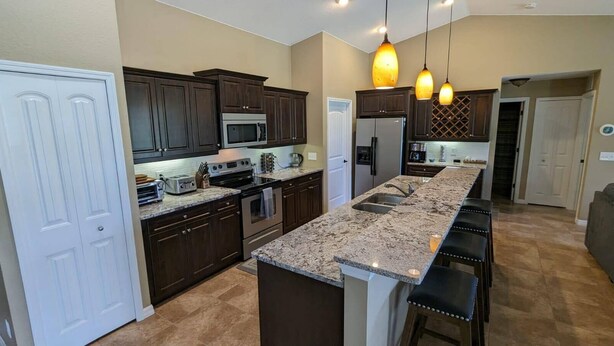 A modern kitchen with dark wood cabinets, stainless steel appliances, a granite countertop, and pendant lighting.