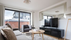 A modern living room with a sofa, armchair, round coffee table, and a flat-screen TV on a stand.