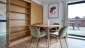 A modern dining area with a wooden table and chairs, a large window with a view, and a sliding wooden shelf unit.