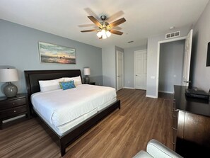 A bedroom with a bed, two bedside tables, a ceiling fan, a painting, and a door.