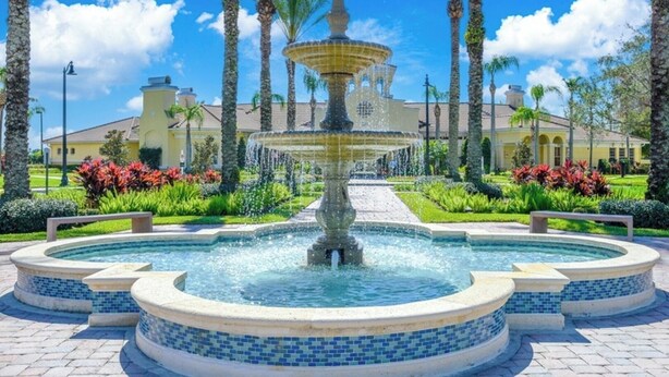 Una fuente de varios niveles en un jardín ajardinado con palmeras y un edificio al fondo.