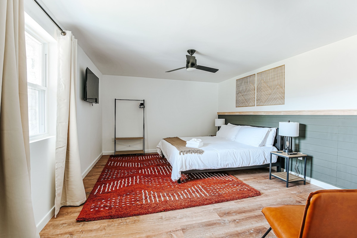 Une chambre d’hôtel avec un lit, un tapis rouge, un ventilateur de plafond, une télévision et une table de chevet avec une lampe.