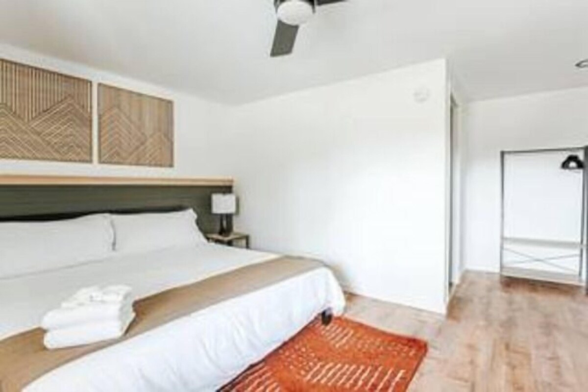 Une chambre d’hôtel moderne avec un grand lit, un ventilateur de plafond et une tête de lit en bois.