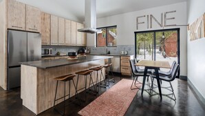 Eine moderne Küche mit Holzausstattung, einem Edelstahlkühlschrank, einer Mikrowelle und einer großen Kücheninsel mit Barhocker.