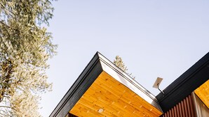 Ein modernes Haus mit Holzfassade, großen Fenstern und einer Terrasse mit Gartenmöbeln.