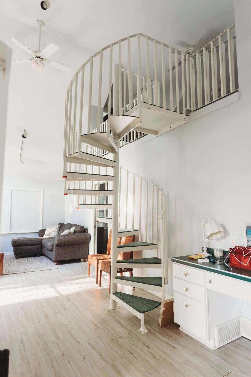 A modern interior with a spiral staircase, a gray sofa, and a desk with a lamp.