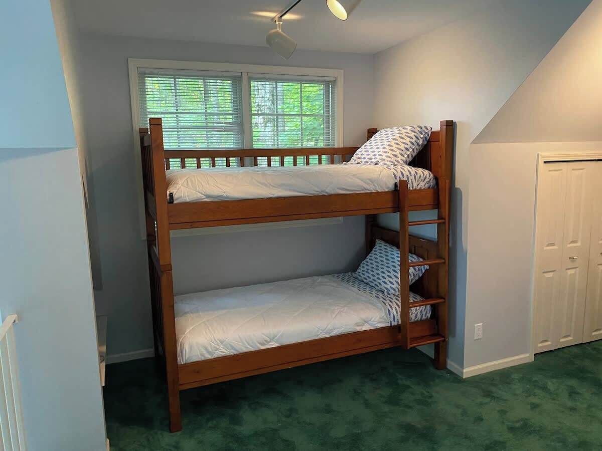 Ein Stockbett in einem Zimmer mit Fenster, Deckenventilator und Tür.