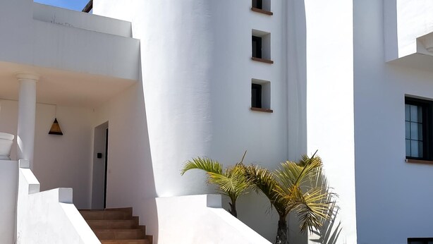 A white building with a staircase leading to a door, palm trees, and a clear blue sky. - Laguna Home by Best Holidays Fuerteventura (Corralejo)