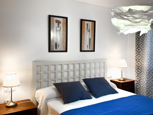 Un dormitorio moderno con una cama grande, dos obras de arte colgadas en la pared, un cabecero blanco y una cortina estampada.