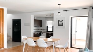 A modern kitchen with dark cabinets, a wooden dining table, and white chairs. - Laguna Home by Best Holidays Fuerteventura (Corralejo)