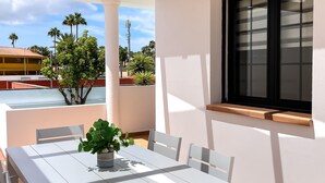 A white table with chairs and a potted plant on a balcony with a view of palm trees and a building. - Laguna Home by Best Holidays Fuerteventura (Corralejo)
