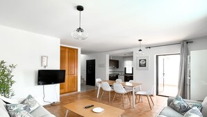 A modern living room with a sofa, a coffee table, a TV, and a dining area with chairs and a table. - Laguna Home by Best Holidays Fuerteventura (Corralejo)
