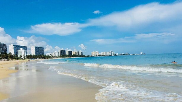 A beach with a clear sky, calm sea, and a city skyline in the background. - Casa LindaMaria 4 mins from the airport 6 mins from isla verde (Carolina)